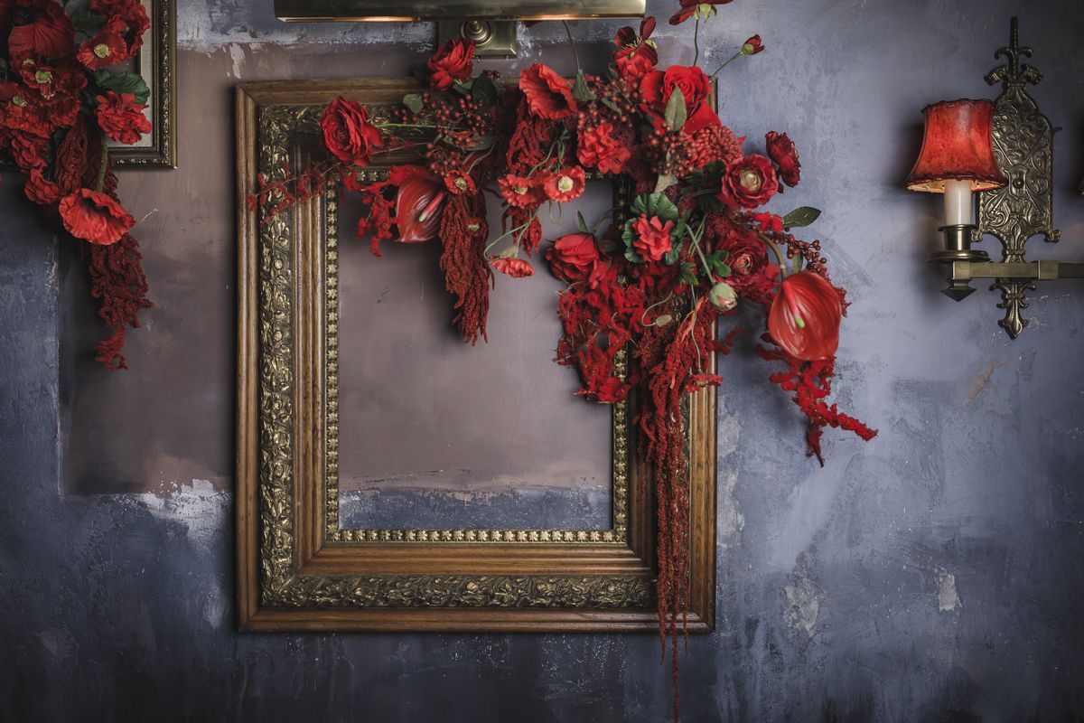 Red roses adorn a purposefully empty picture frame set against a dark wall.