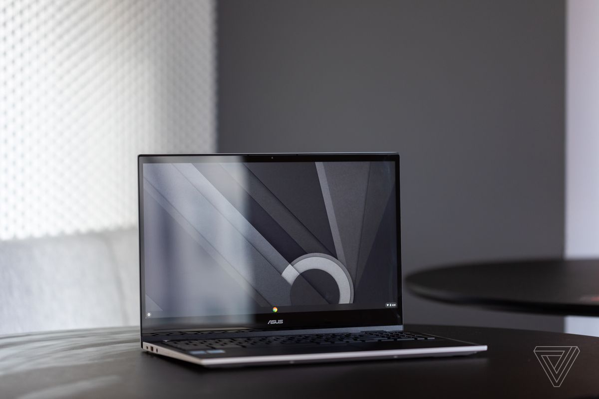 The Asus Chromebook CX5 open, angled to the right, on a table with a gray and white background.  The screen shows a black, white and gray desktop pattern.