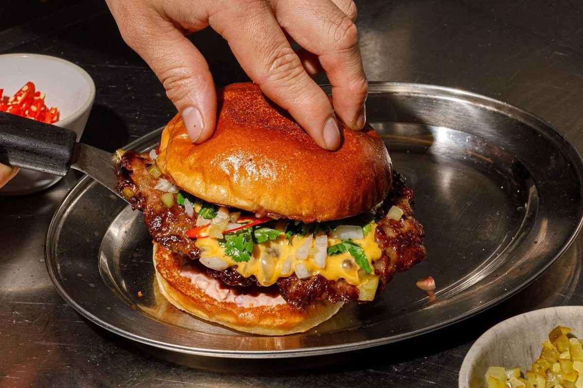 A chef plates a smashburger with cheese and chilli on a metal platter