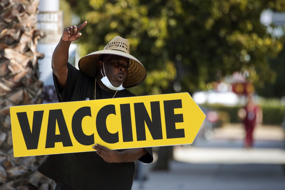 A man holding a yellow sign that says “vaccine” directs people towards a mobile Covid-19 vaccine clinic in Los Angeles, California.