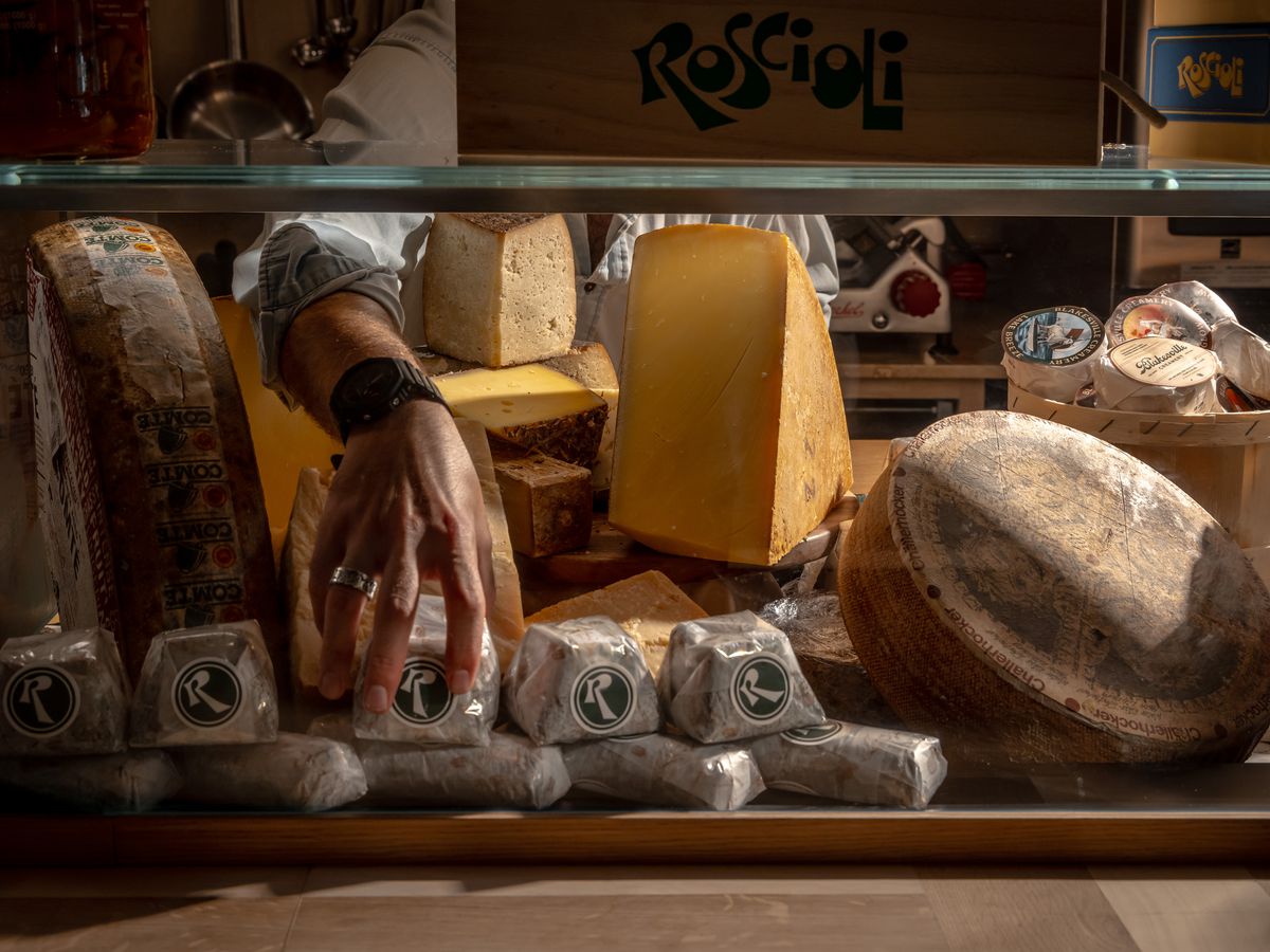 A hand grabs cheeses from Roscioli’s cheese case.