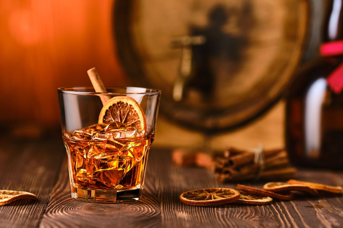Glass of cocktail with whisky and orange liquor with barrel on background.