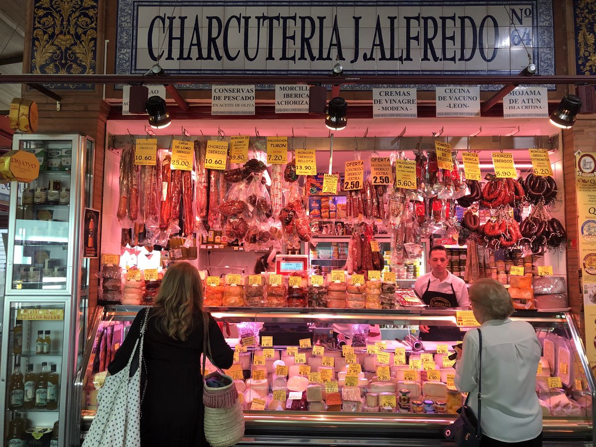 Two customers stand in front of a deep red charcuterie stall.