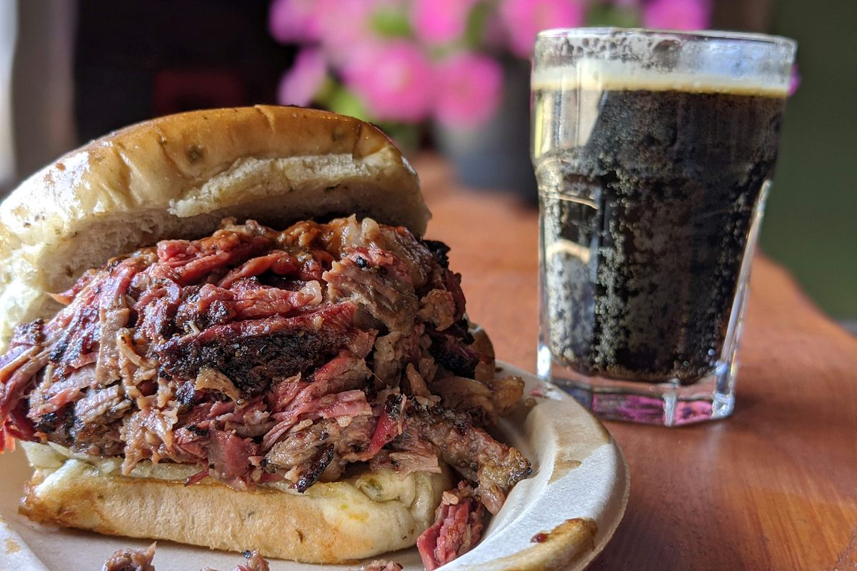 A barbecue sandwich next to a glass of soda.