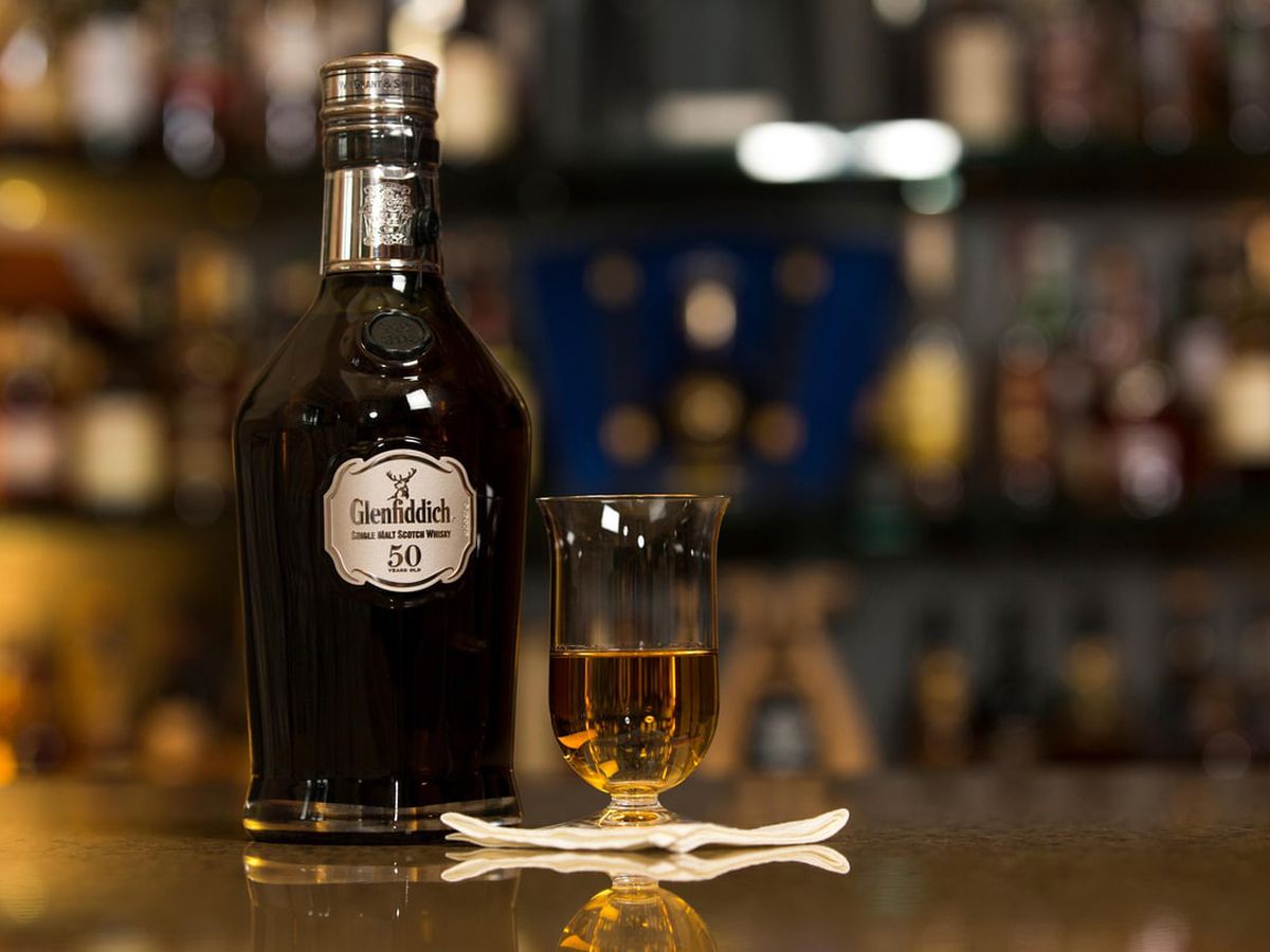 A bottle of Glenfiddich next to a snifter glass of Scotch.