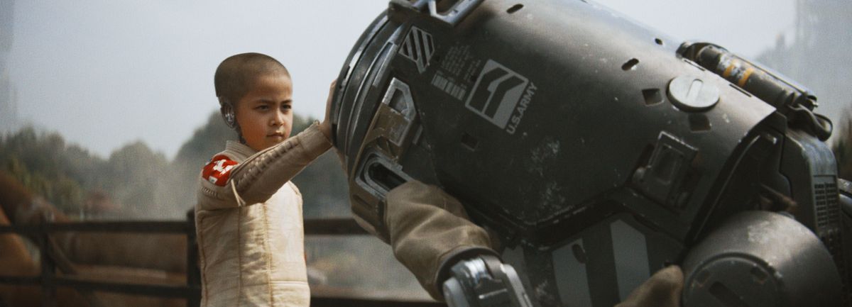 a young cyborg girl with a shaved head places her hand on a trash-can-like robot bowing to her in The Creator
