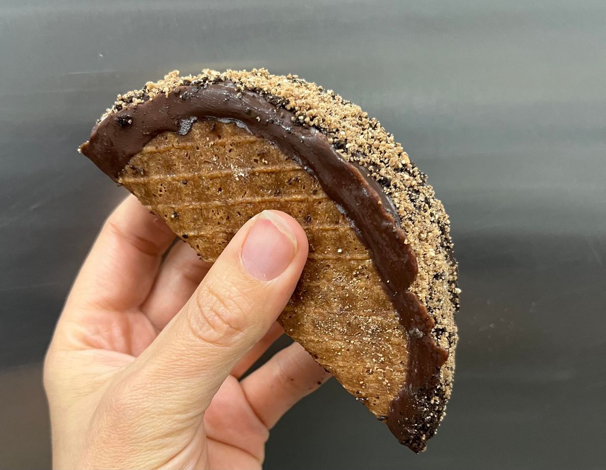 A hand holds a restaurant-made version of a Choco Taco dipped in chocolate and rolled in a crumb coating.