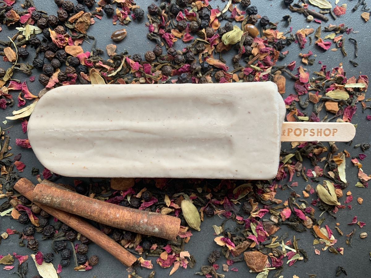 An overhead few of a traditional popsicle with a stick that says Lil Pop Shop, surrounded by cinnamon sticks and rose petals.