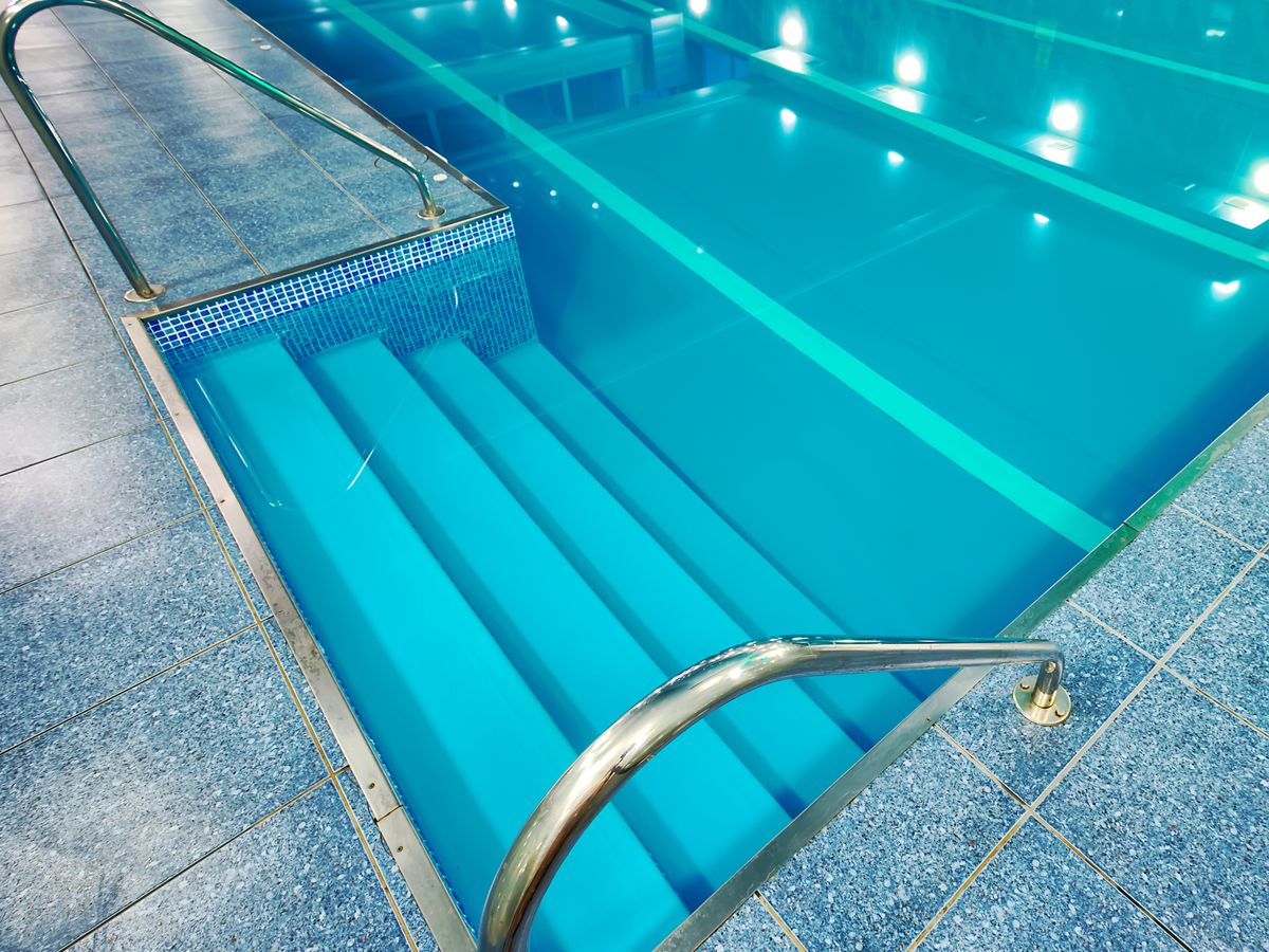 A handrail and stairs going into an indoor swimming pool