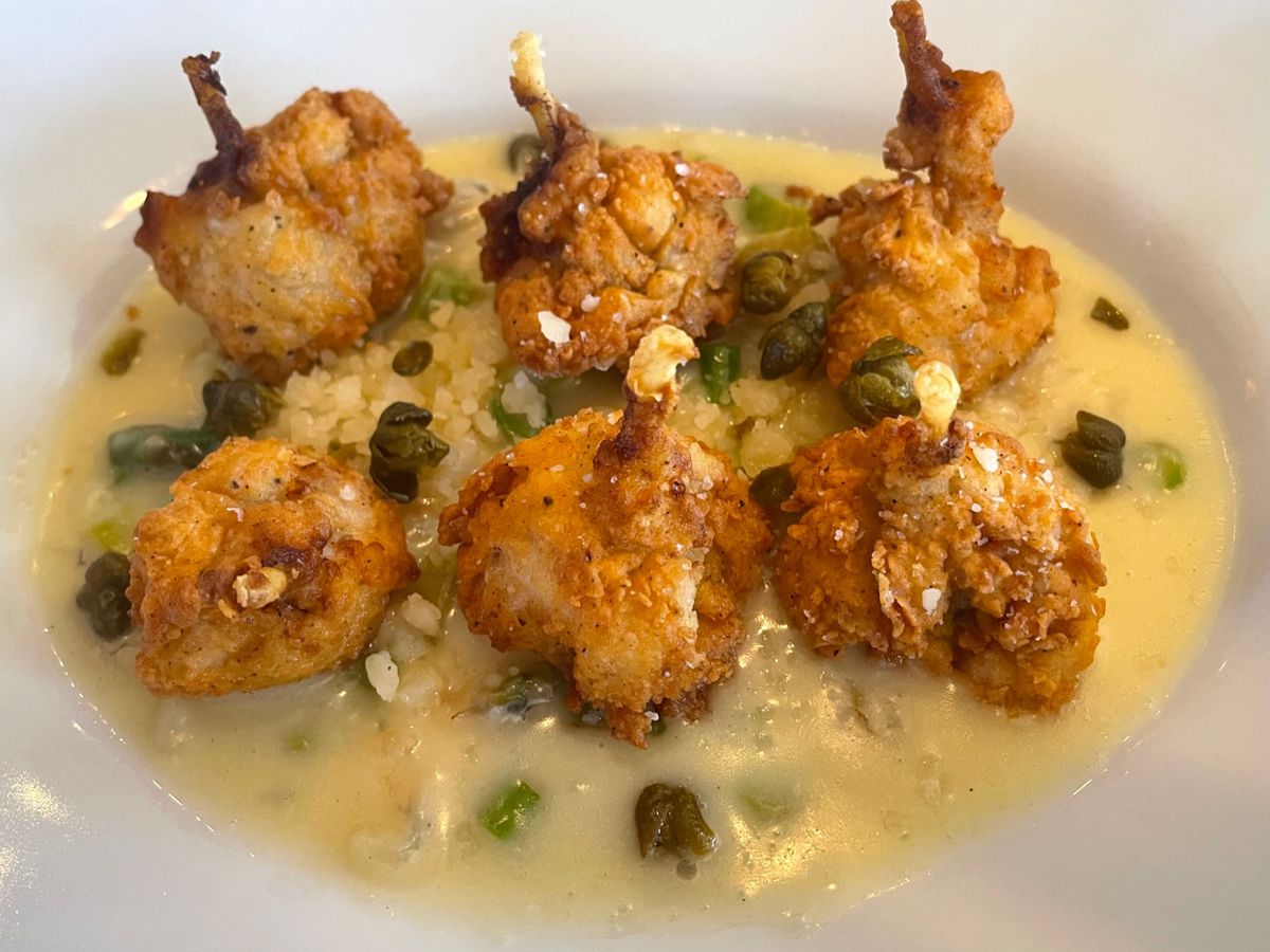 Six golden breaded and fried frog legs over Parmesan risotto dotted with deep green chunks of asparagus and caper spheres.