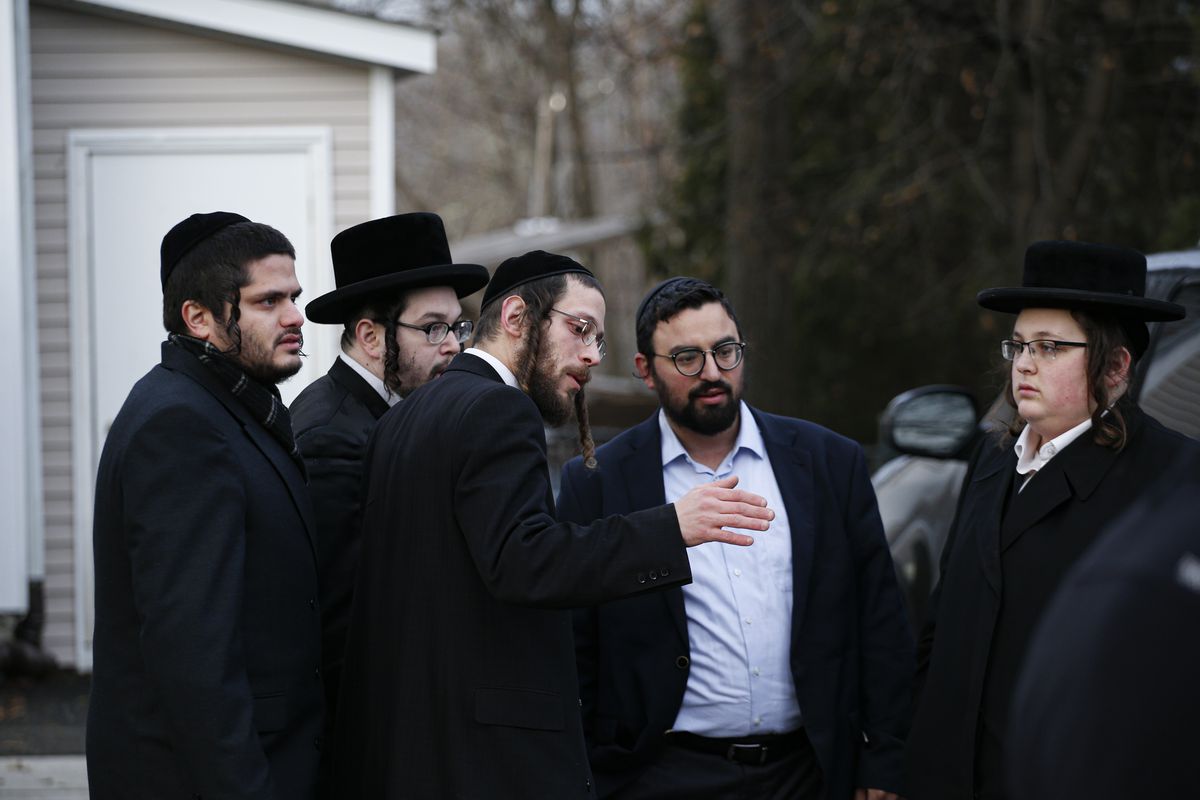 Men in Orthodox Jewish attire stand outside a house and talk to one another.