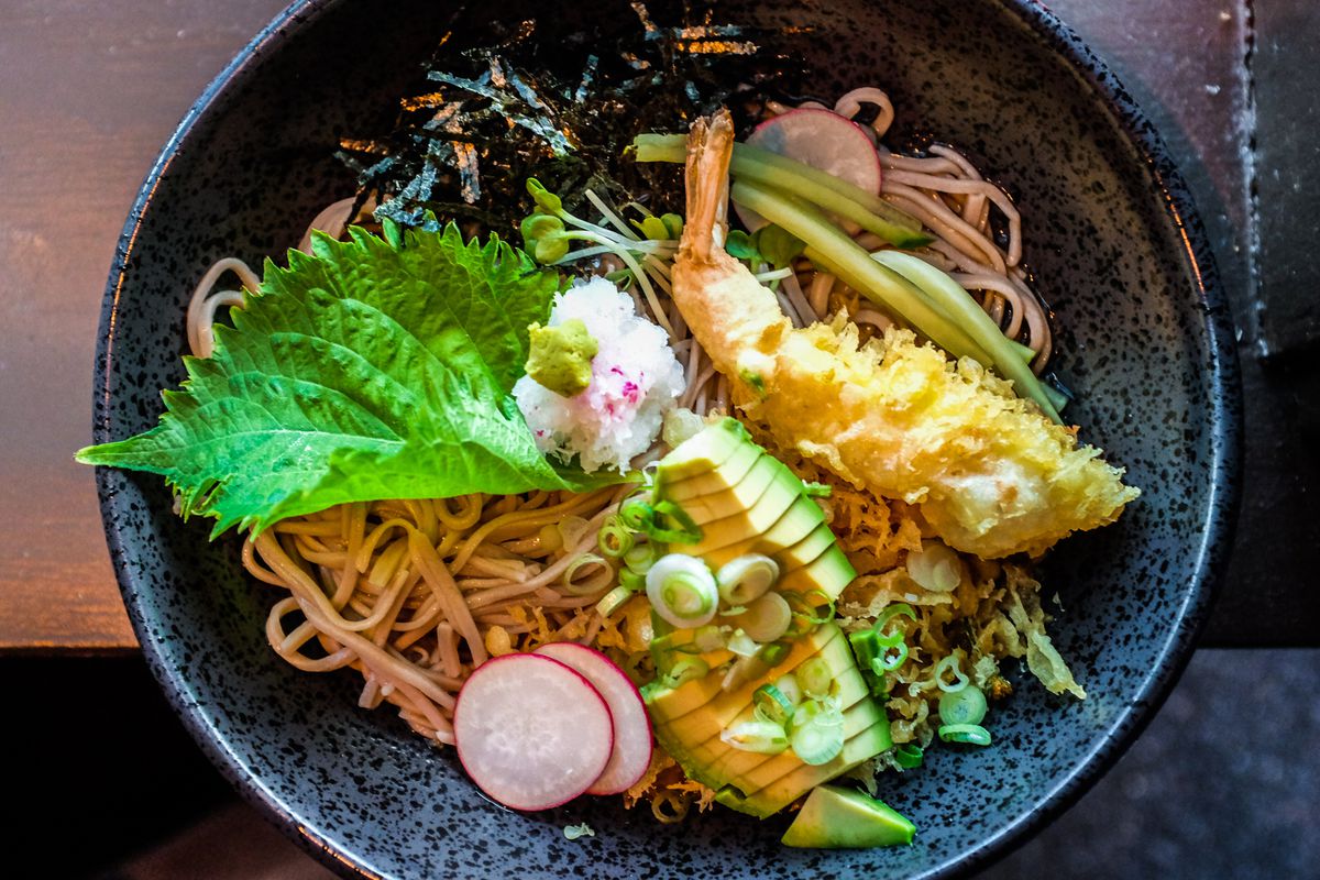 A bowl full of soba noodles, topped with sliced avocado and shiso leaf.