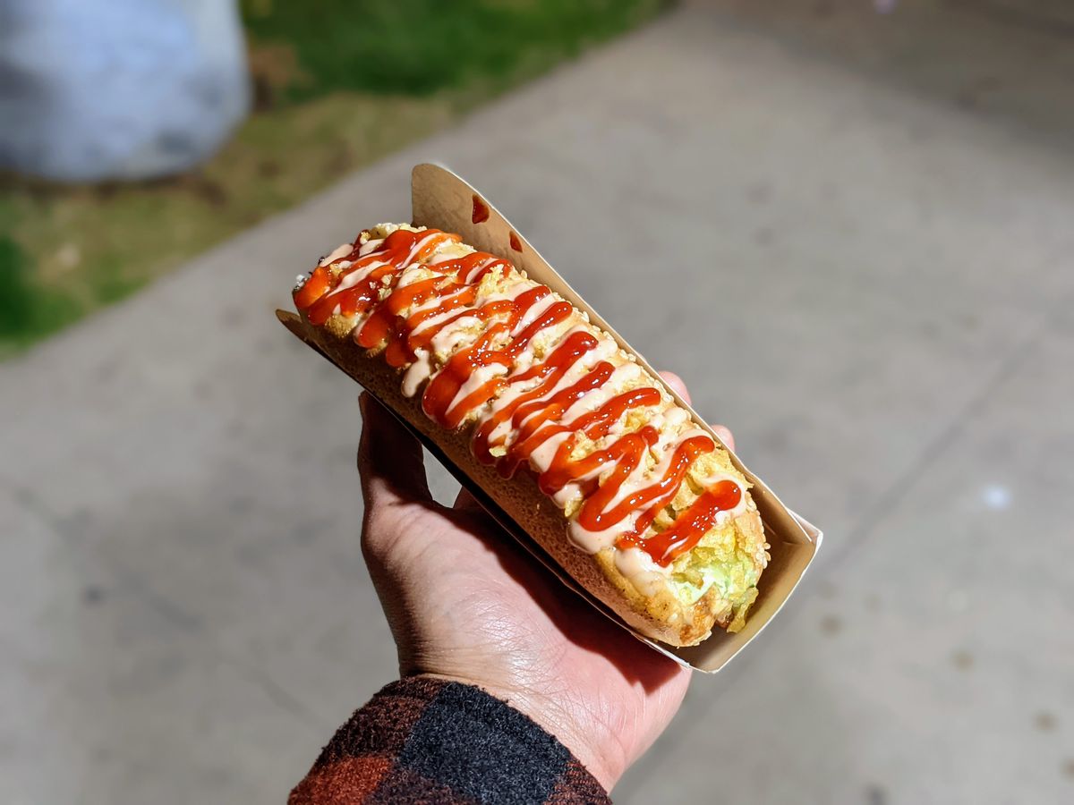 A hot dog topped with drizzles of several different sauces at Vivi’s Gourmet Cuisine.