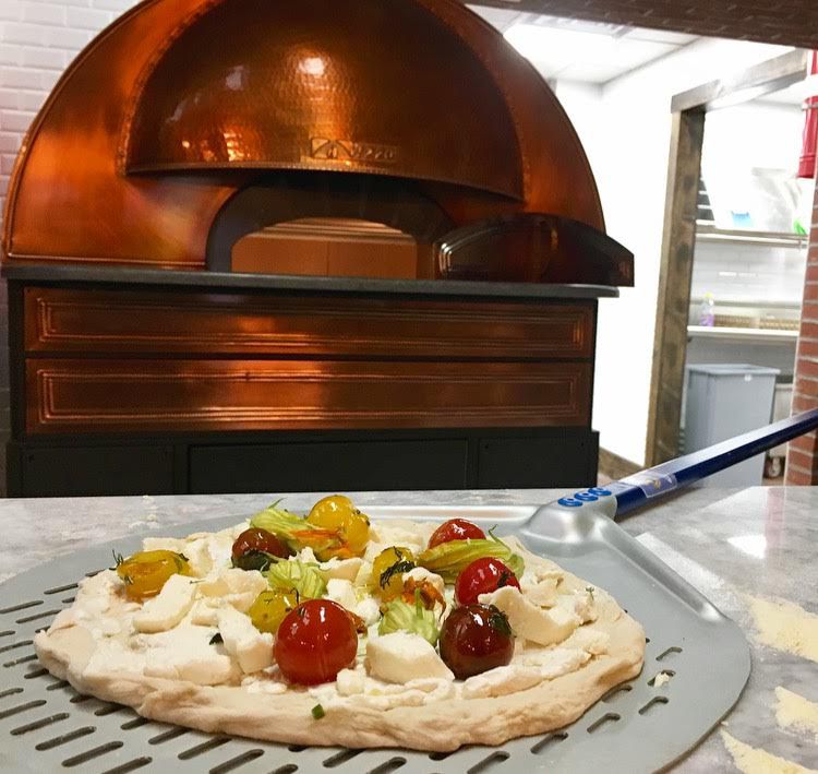 A Keste pizza dough with tomatoes on it, in front of an oven.