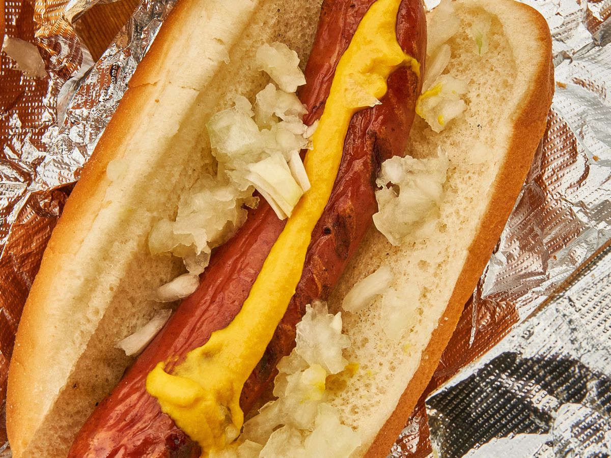 A grilled hot dog on a toasted bun with mustard and chopped onions.