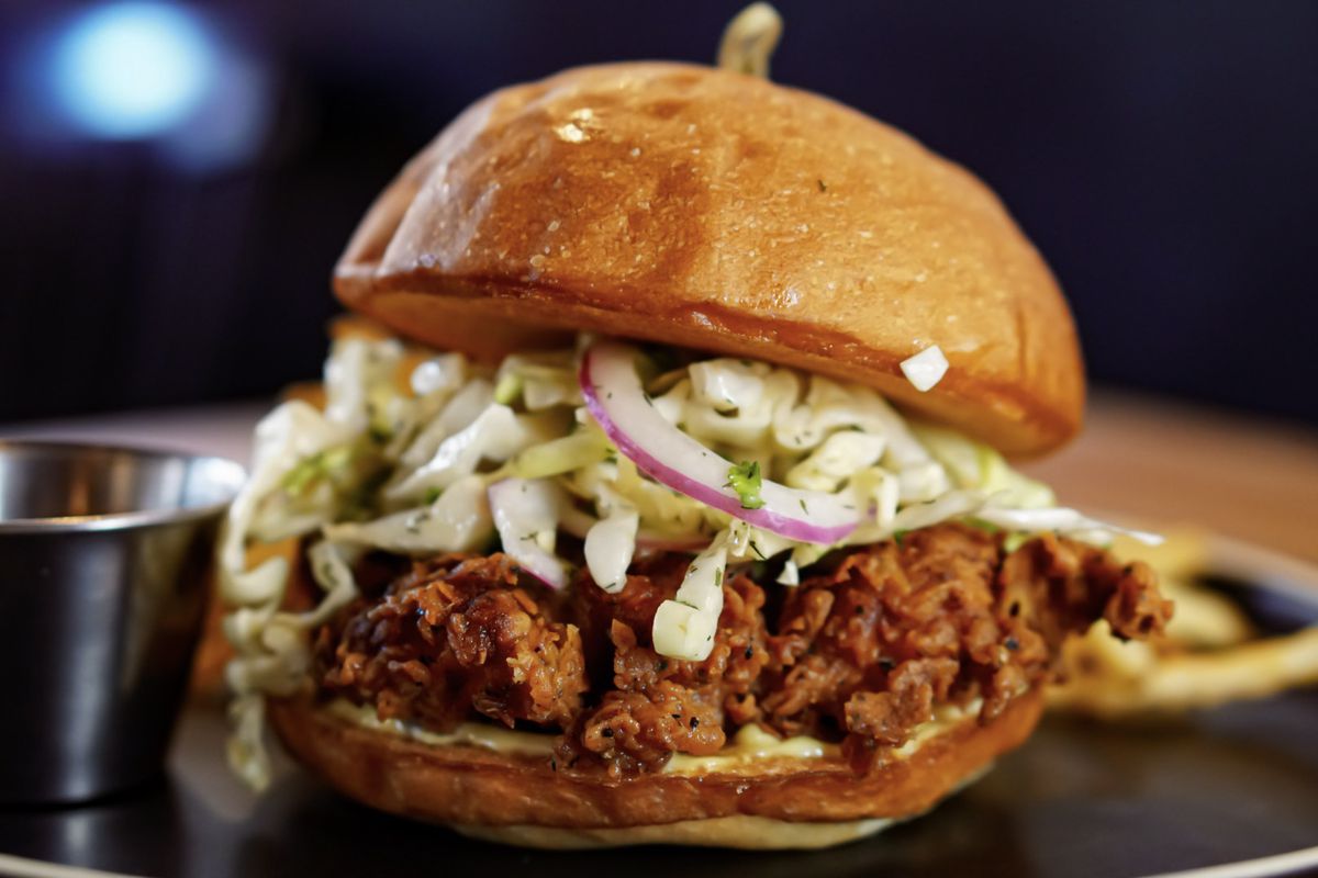 A fried chicken sandwich, loaded with toppings like coleslaw and red onion, on a toasted bun.