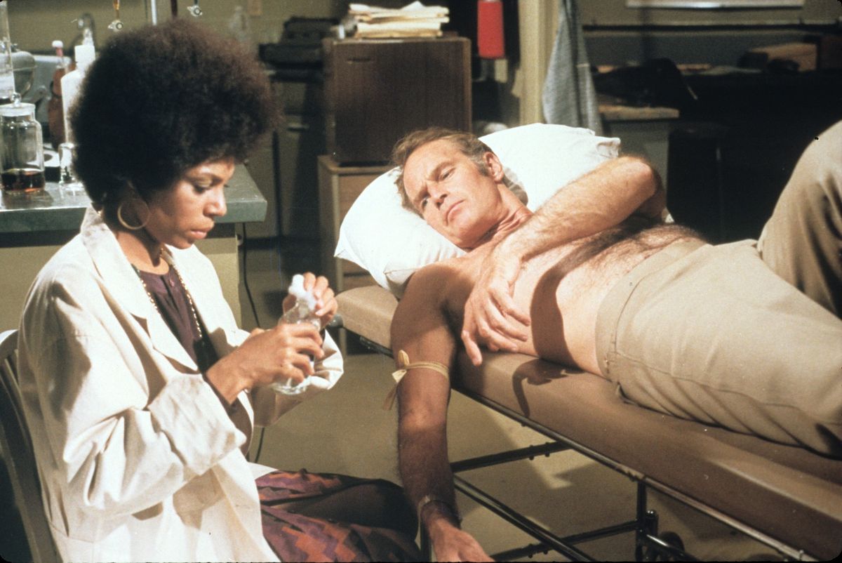 A nurse prepares an infusion for a man on a gurney.