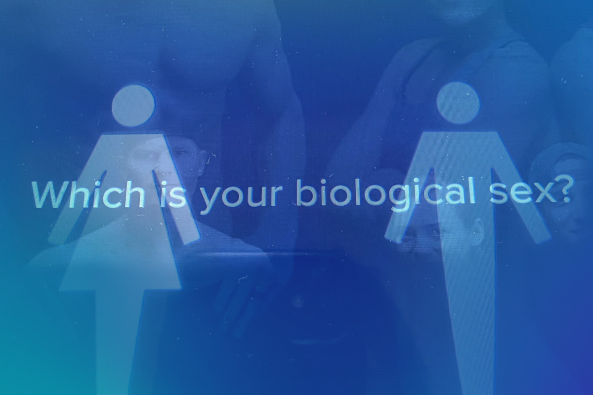 On screen display shows a figure representing female and male bodies and words that say “Which is your biological sex?”