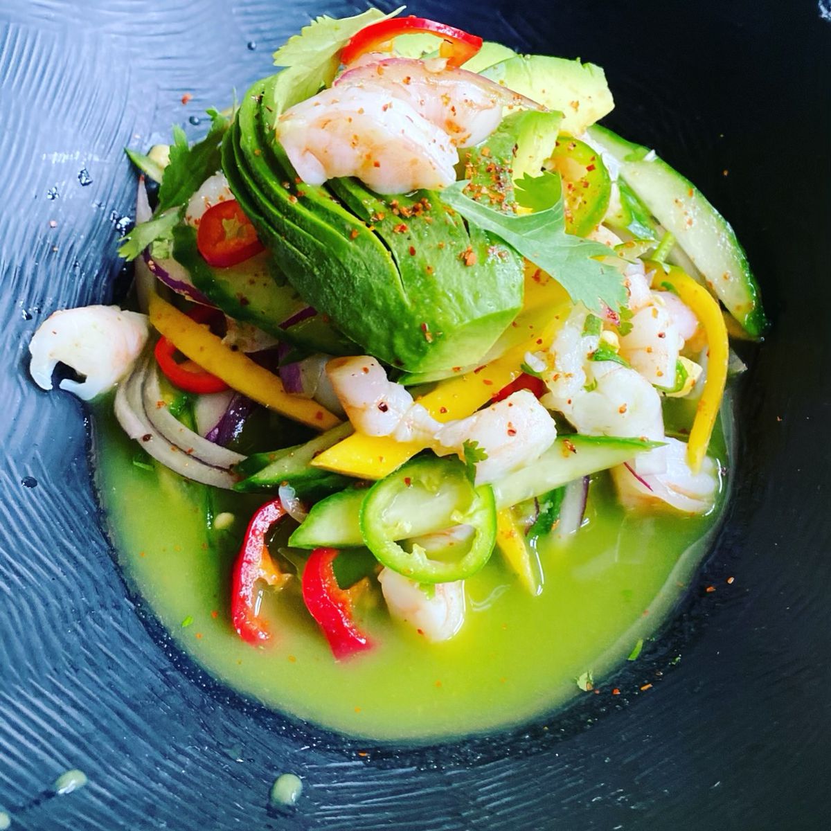 Shrimp ceviche with avocado and vegetables in a green sauce in a black bowl.