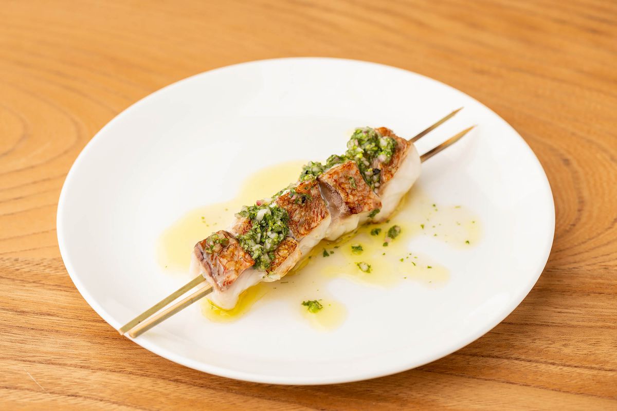 Two skewers run through cooked pieces of fish with skin on at a new restaurant, at daytime.