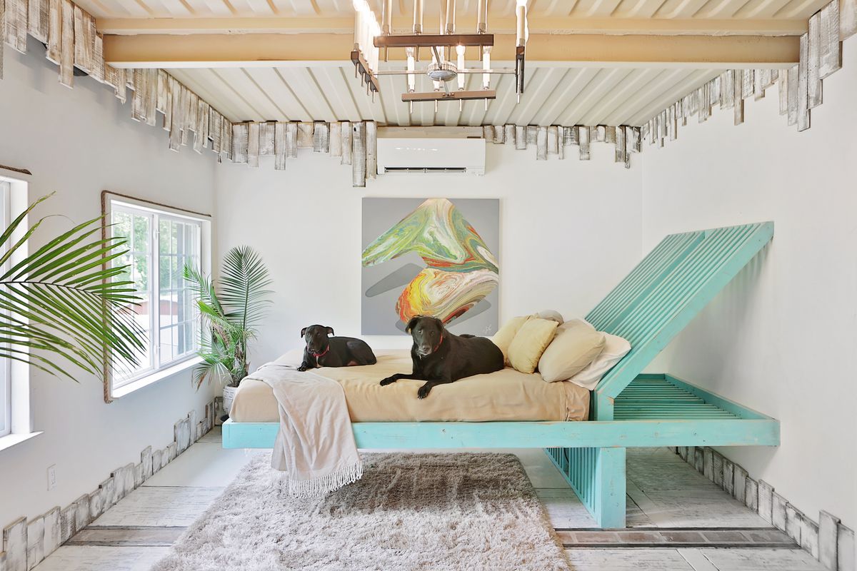 Salvaged wood is used to make an unusual bed whose foot floats above the floor and whose head has a sharp slope. The whole thing is painted aqua and two black dogs (a pit bull named Boomer and a labrador named George) lie on the bed.