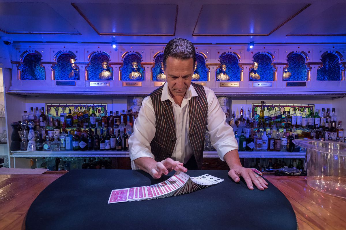 A worker at Hollywood’s famed Magic Castle shuffles a line of cards on a piece of felt inside a blue room.