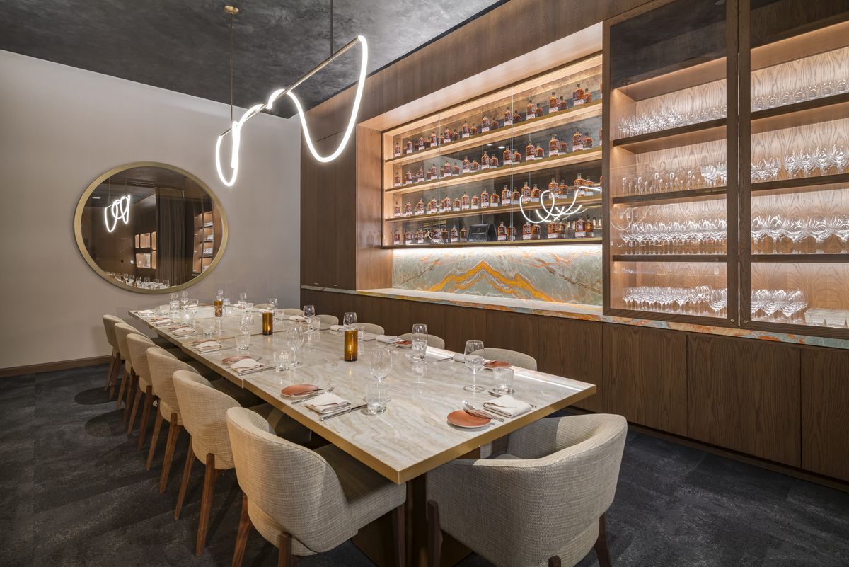 A carpeted private dining space with upholstered dining chairs and a wall lined with glass cabinets holding a collection of whiskey bottles.