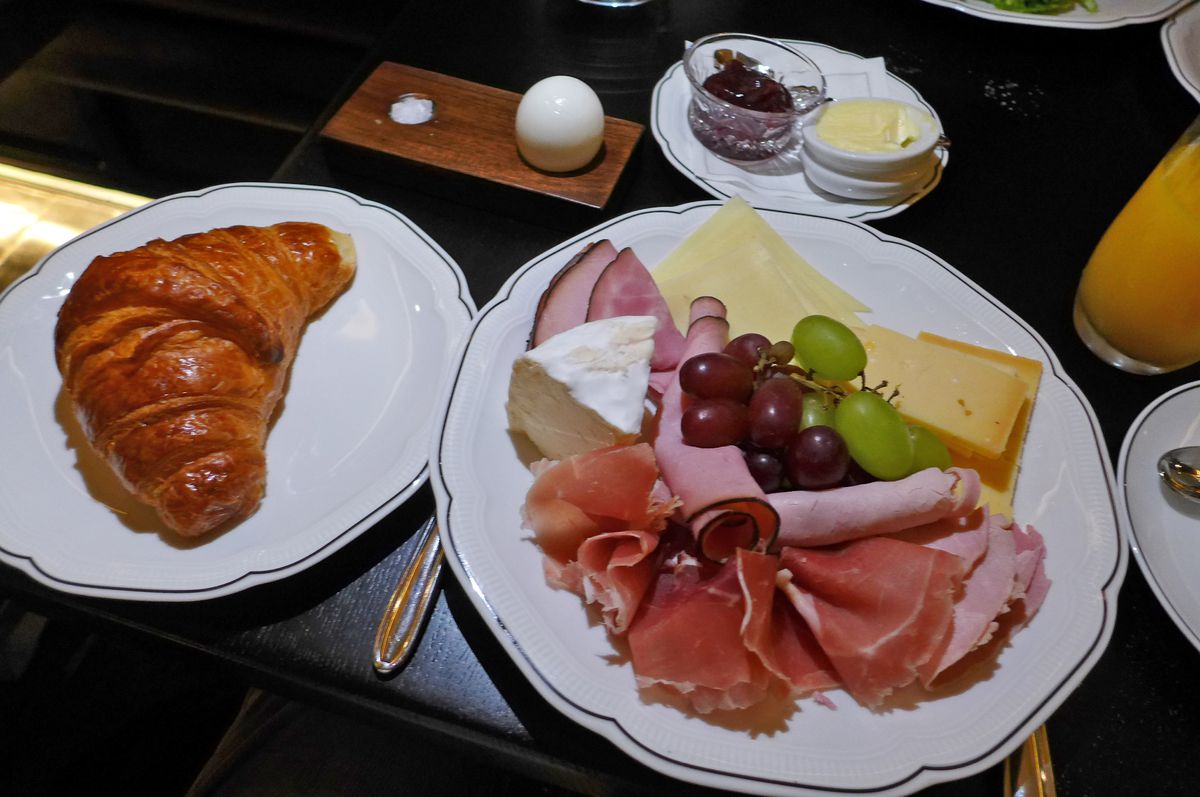 A plate with sliced meat and cheese and satellite plates with other dishes.
