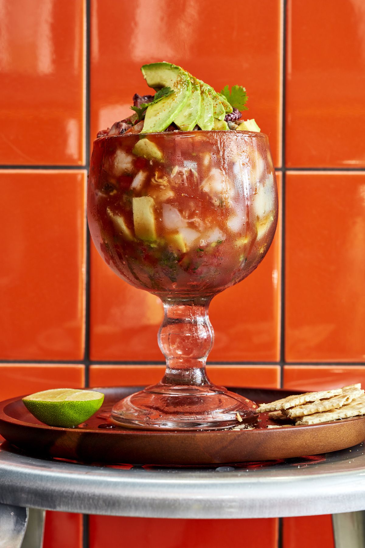 A goblet of ceviche against a red tiled background.