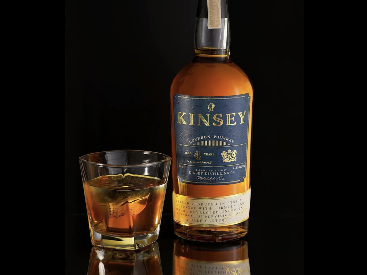 A tall bottle of Kinsey Whiskey alongside a glass of whiskey on the rocks.