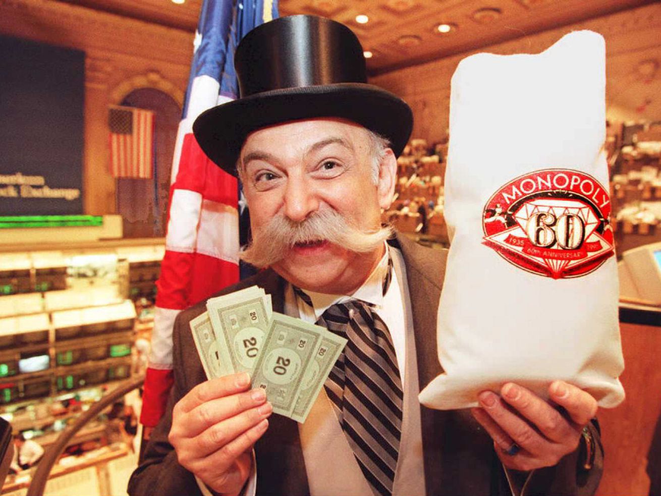 A person dressed up as Mr. Monopoly, holding up Monopoly money and a money bag commemorating the 60th anniversary of the game.