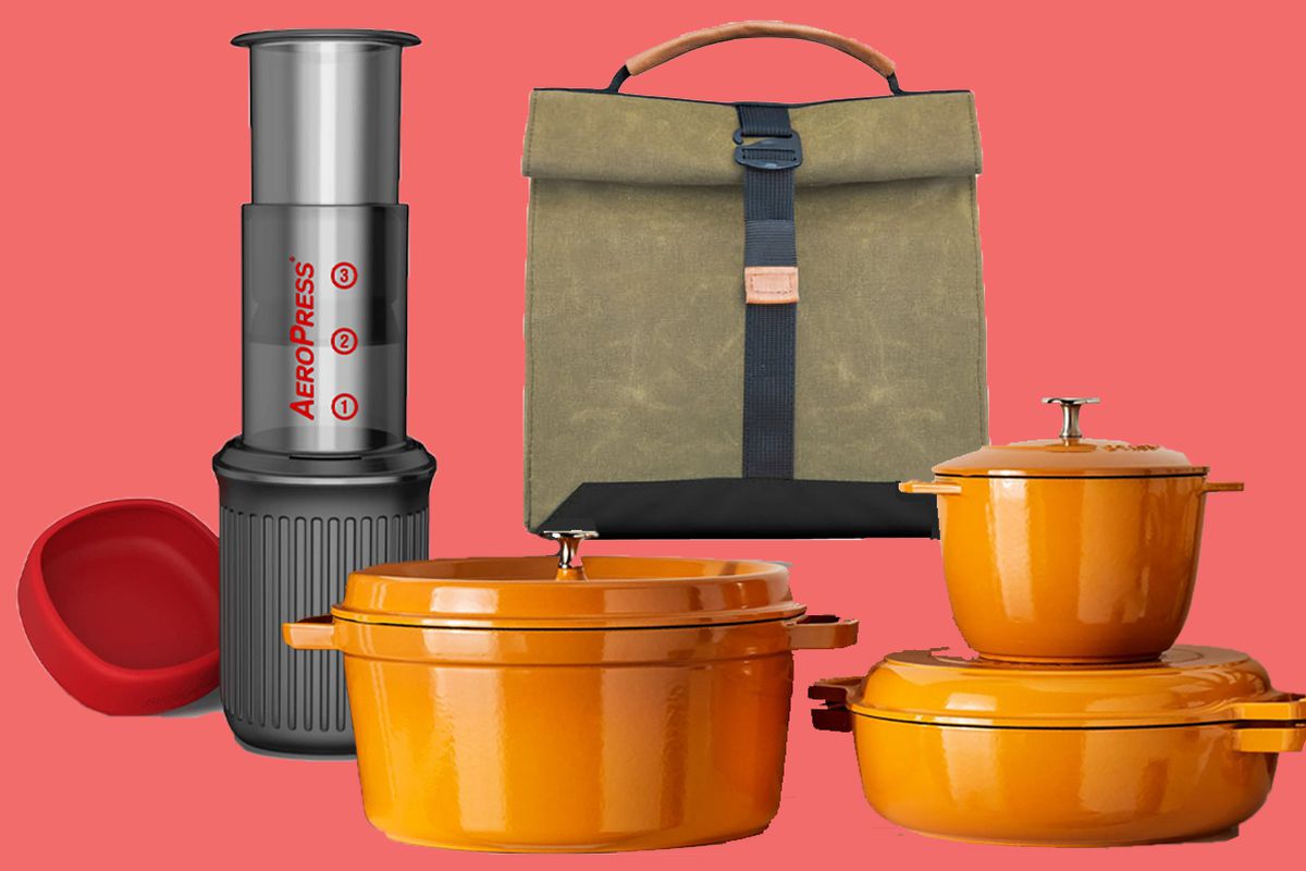 An Aeropress coffee machine, a army-green canvas bag with top-handle, and a set of pumpkin-colored Staub pots, all on a pink background