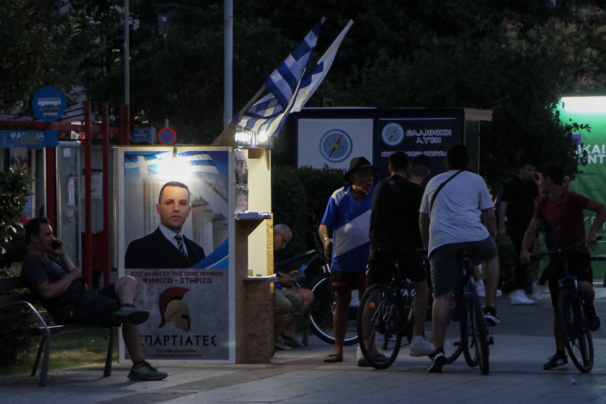 People stand around a booth of the far-right party Spartiates (Spartans) showing a portrait of ultra-nationalist Ilias Kasidiaris, in a square in the southern Greek city of Kalamata, on June 25, 2023.