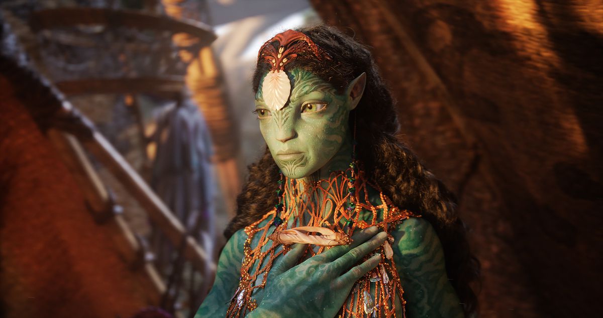 Kate Winslet as Ronal in Avatar: The Way of Water, wearing a headdress and body adornment made of shells and other sealife, while holding her finned hand to her chest