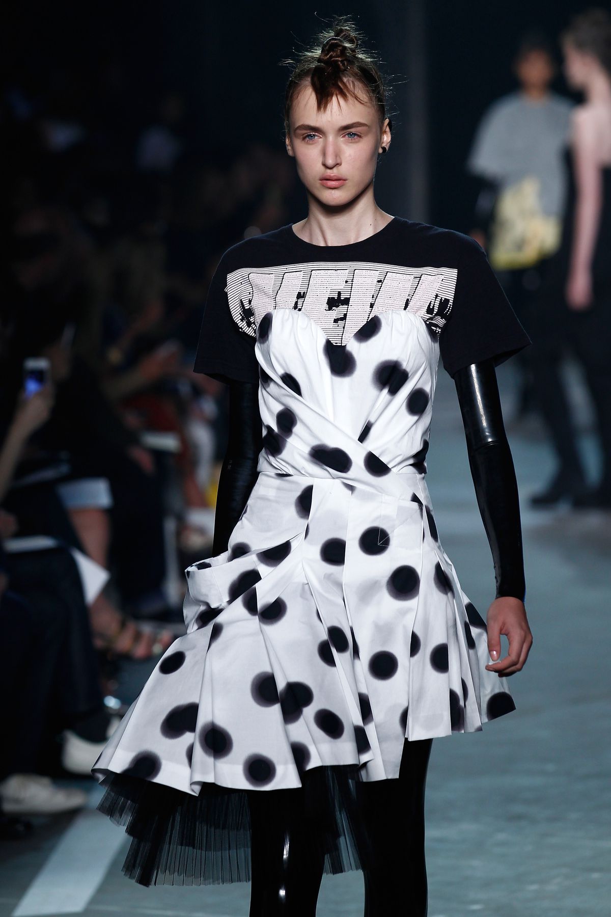 A model wears a latex bodysuit under a girly polka dot dress.