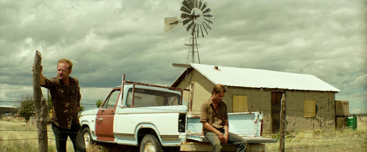 Chris Pine sits on the back of a pickup truck as Ben Foster leans against a piece of wood in Hell or High Water.