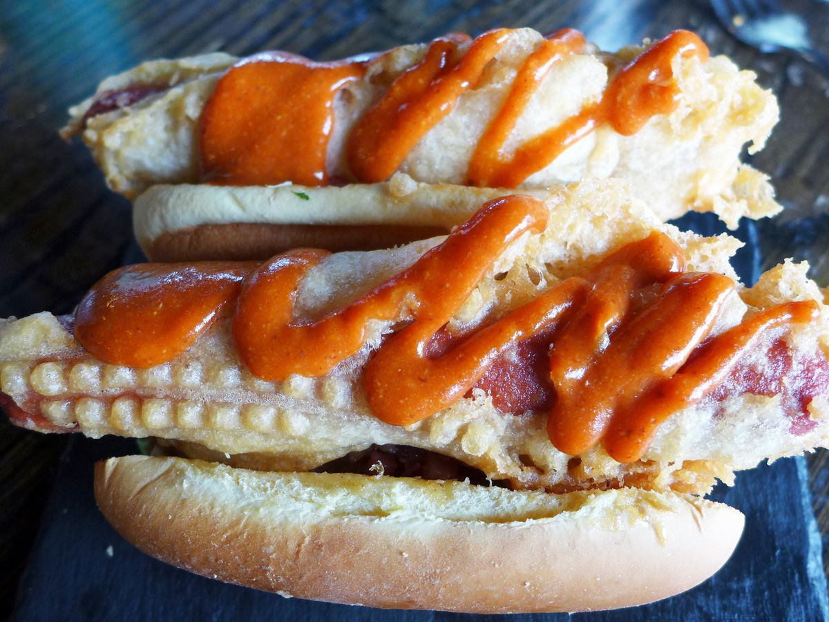 Two batter covered dogs in buns with red sauce.