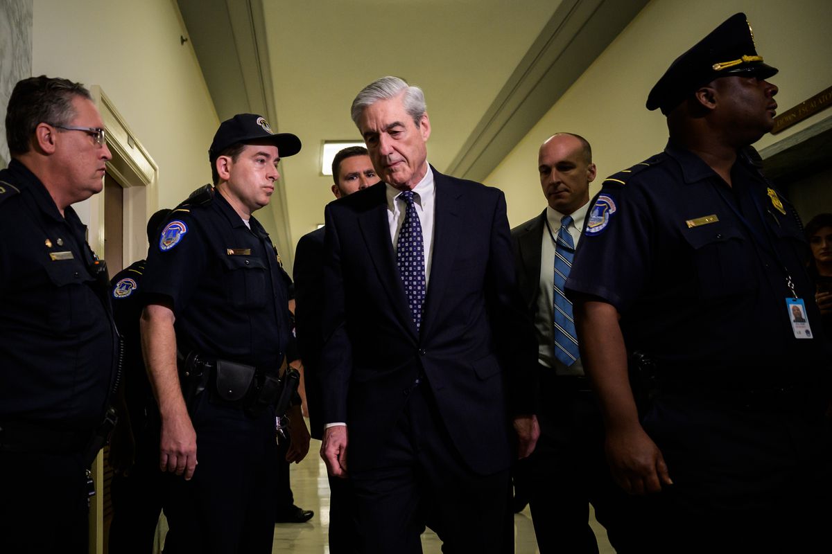 Robert Mueller walks down a hallway lined with uniformed police officers.
