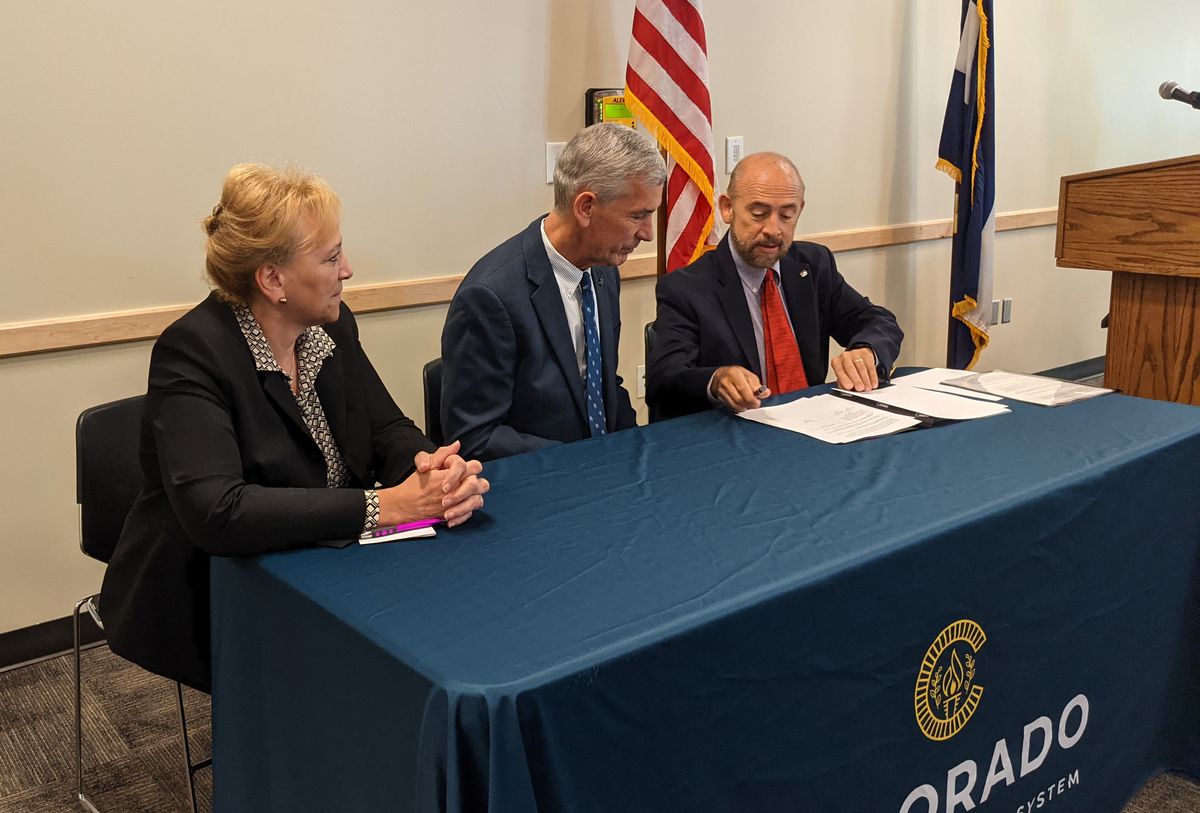 Three Colorado college leaders dressed in suits sit at a table with blue cloth to sign a document that formalizes a partnership between community colleges and the Colorado School of Mines.