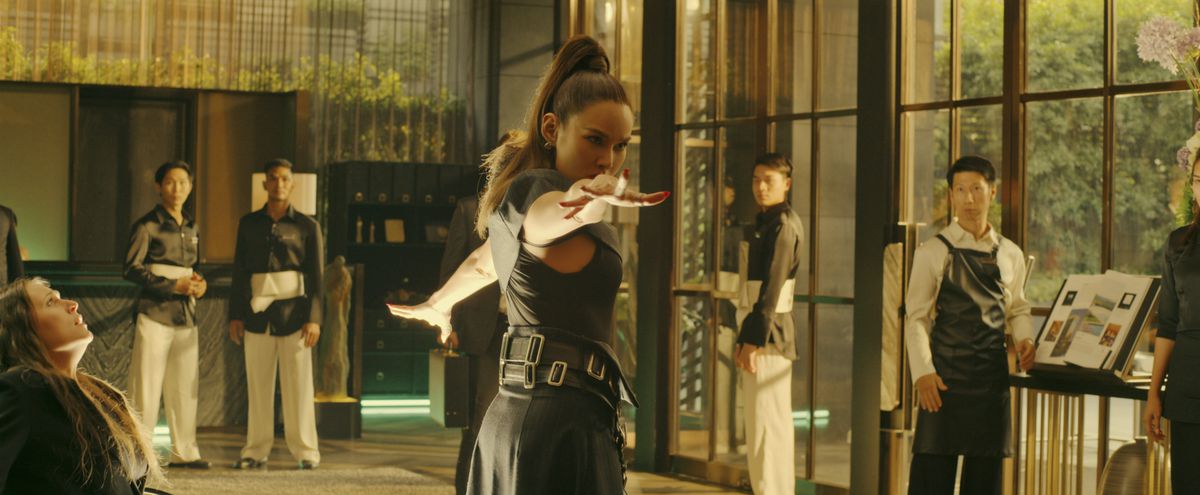 Rhatha Phongam as Ku An Qi gestures dramatically in a glass-walled dojo in Fistful of Vengeance