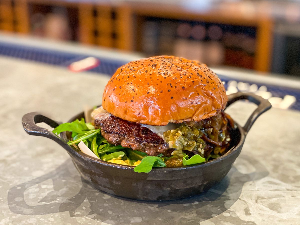 A tall burger in a deep cast iron pan on a bar top.