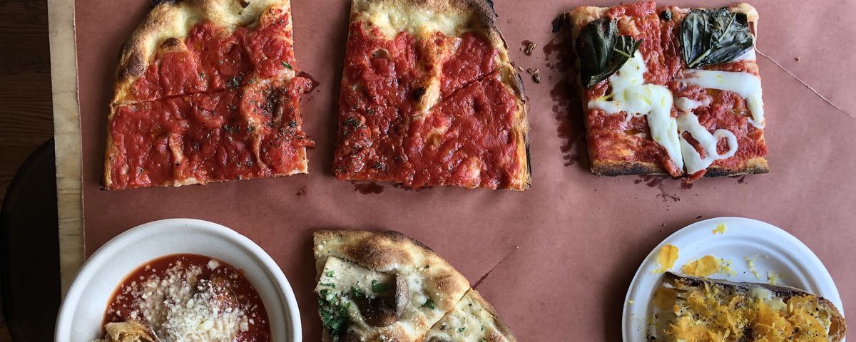 A spread of dishes, including tomato pizza, margherita pizza, meatballs, and bottarga toast, sits on a sheet of red butcher’s paper at Bread &amp; Salt in Jersey City