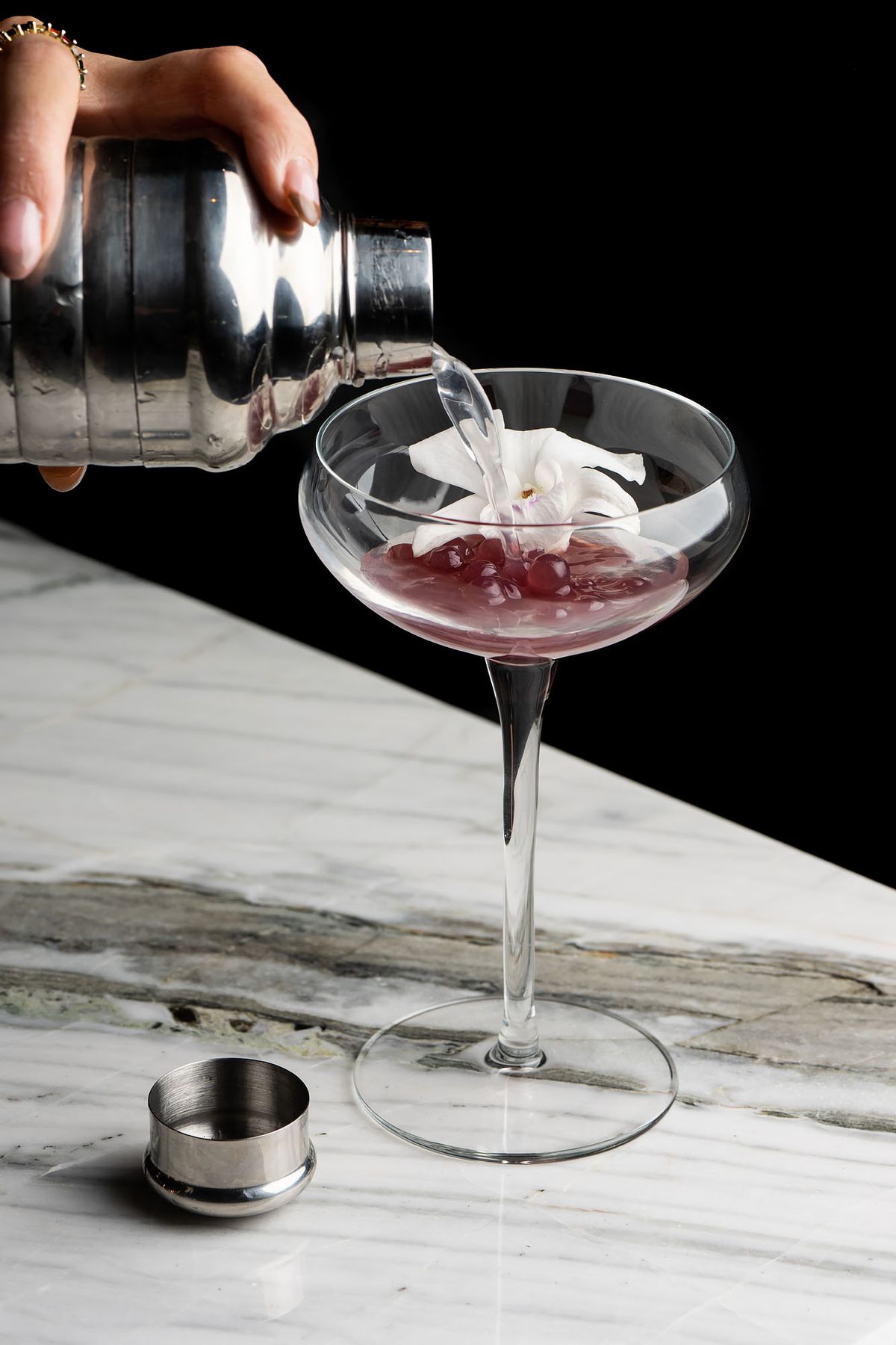 A clear liquid poured over pomegranate in a glass cocktail piece.