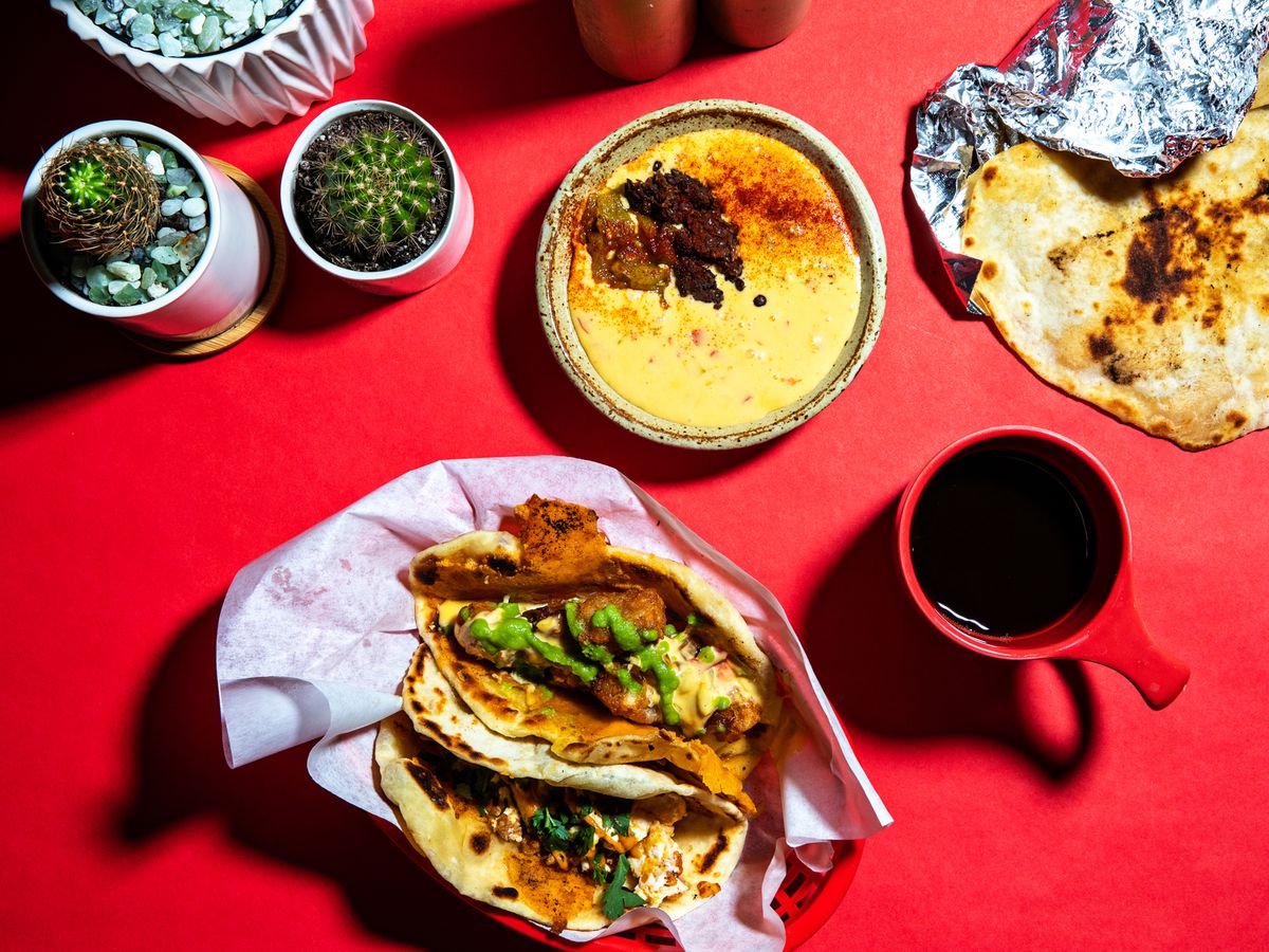 an overhead view of tacos, a mug of coffee, and other dishes and cactuses on a bright red surface