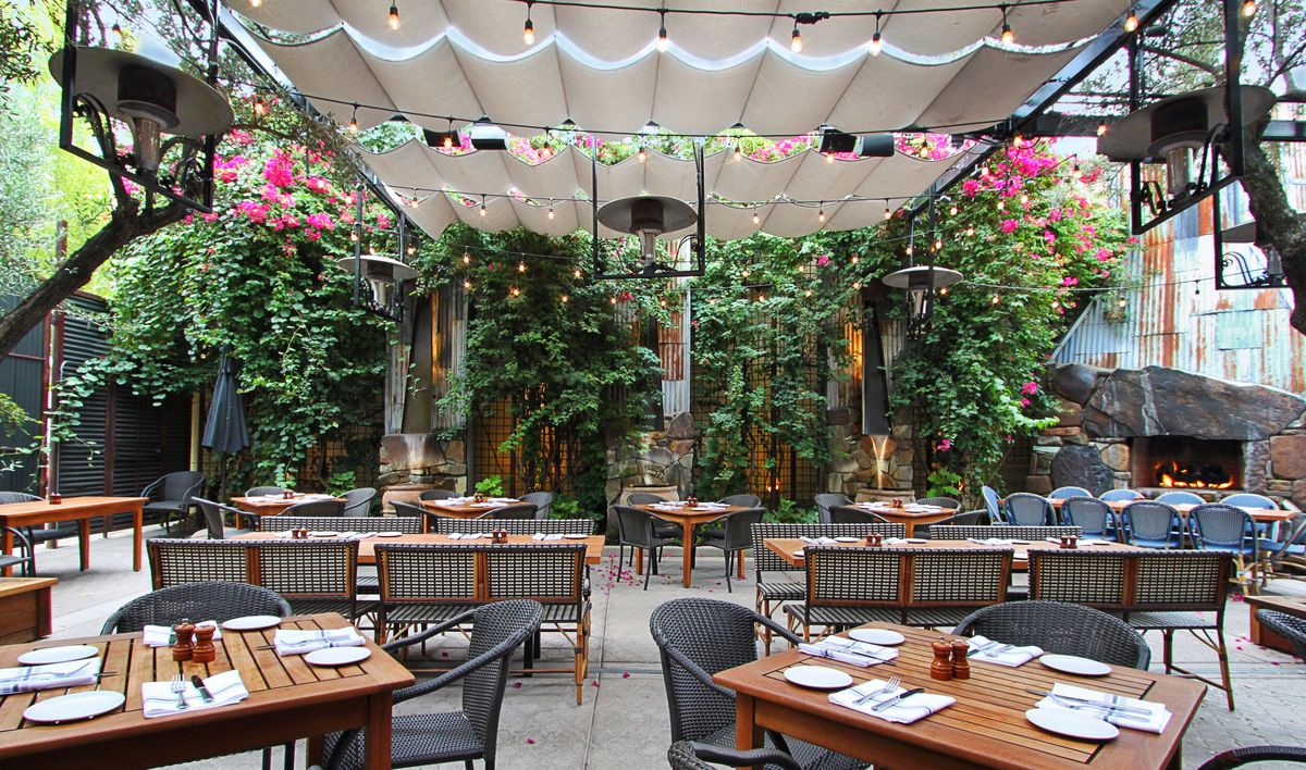 The back patio at Paragary’s, with several wooden tables and black chairs laid out against a backdrop of greenery and underneath a canopy with string lights.