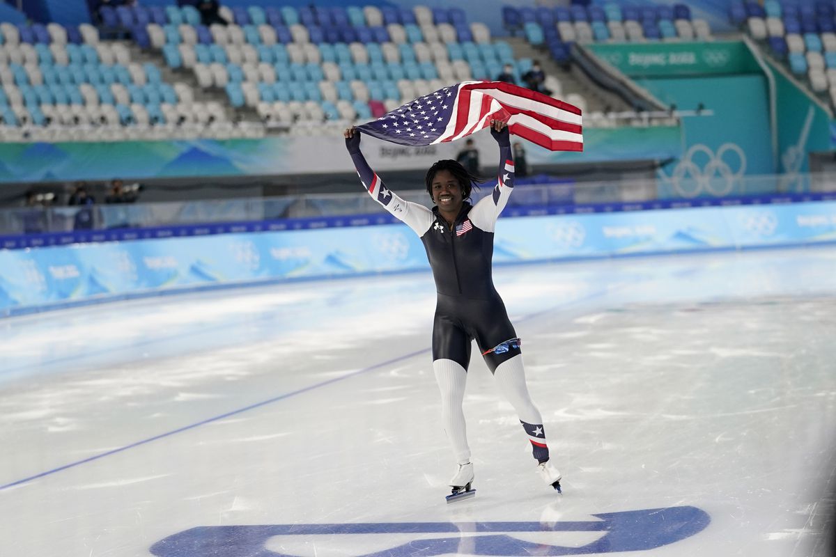 Erin Jackson of the United States smiles while skating on the ice while raising an American flag