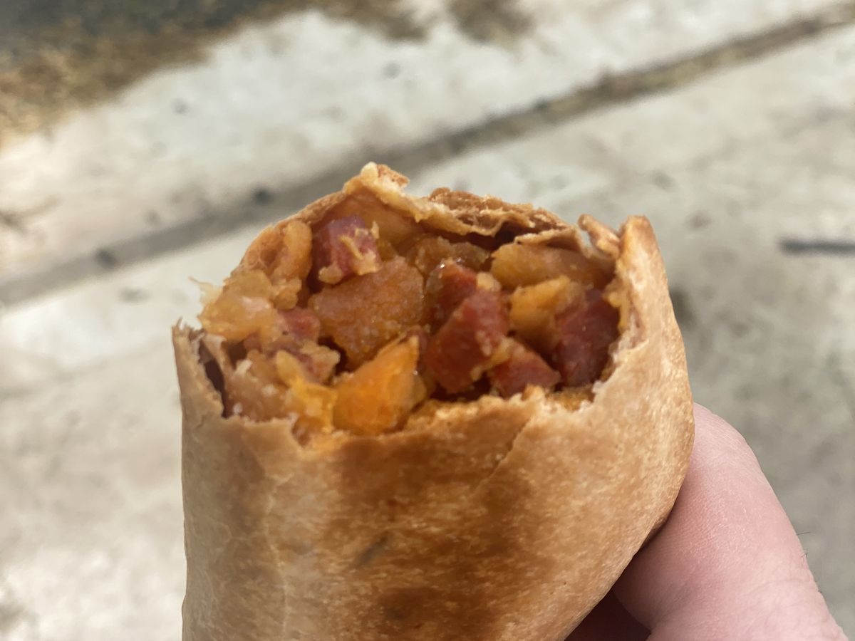 A customer holds a chorizo empanada upright; it’s filled with orange potatoes and red cubes of sausage