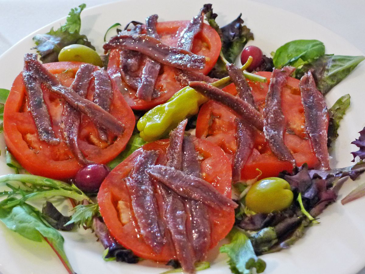 Slices of red ripe tomato with dark anchovies draped across them.
