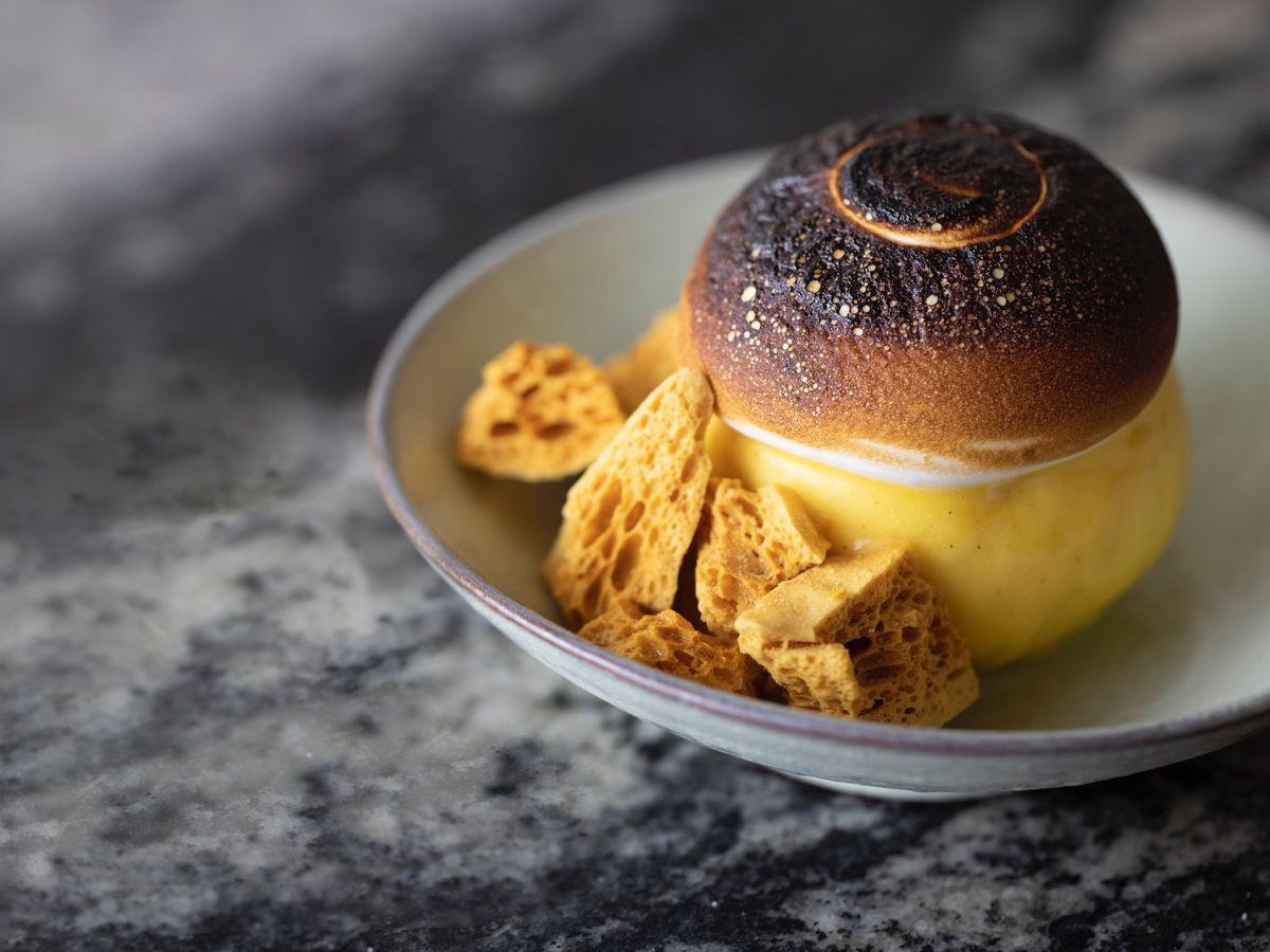 A sundae with a burnt, crispy top sits in a shallow bowl with bits of honeycomb candy served on the side.