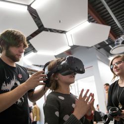 Jared Schrock, left, and Tasha Firth, right, outfit Gracie Lachowsky, 9, with a virtual reality headset so she can try out a game they created, “The Rose Chamber,” at the EAE Play! showcase of games created by the Entertainment Arts & Engineering video game development program at the University of Utah in Salt Lake City on Friday, Dec. 9, 2016.